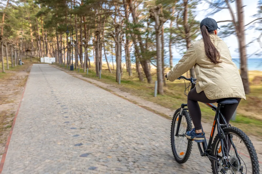 Frau fährt mit dem Fahrrad auf einem Weg an der Küste mit Wald im Hintergrund
